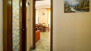 A hallway leading to a dining area with a table and chairs, a clock on the wall, and a painting of a mountain landscape.