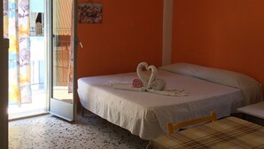 A bedroom with an open door leading to a balcony, a bed with a swan towel decoration, an air conditioner, and a small painting on the wall. - Apartaments Cavour 4 (Cefalù)
