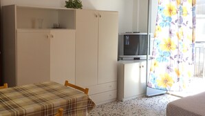 A room with a dining table, chairs, a TV on a cabinet, a wardrobe, and a floral curtain. - Apartaments Cavour 4 (Cefalù)