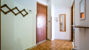 Un pasillo con una puerta de madera, un espejo y suelo de baldosas.