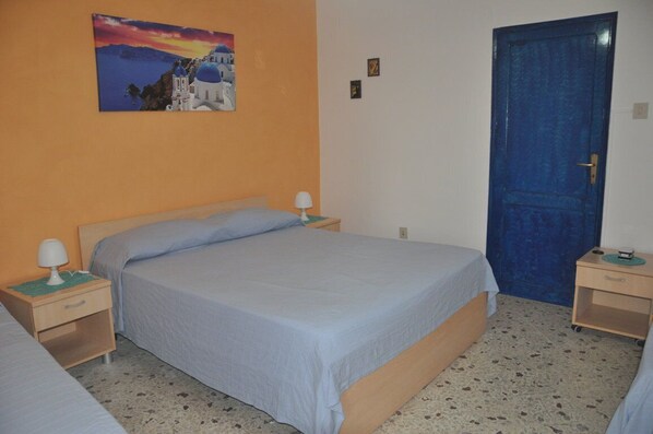 A bedroom with a bed, two bedside tables, a nightstand, a blue door, and a wall painting.