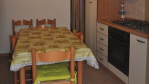Un comedor con una mesa preparada para cuatro, una cocina con estufa y horno, y una lámpara colgante.