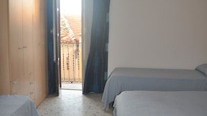 Un dormitorio con dos camas, un armario y vistas a un tejado de tejas por una puerta abierta.