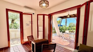 Una habitación con una mesa y sillas de madera, un sofá y ventanas amplias que dan al exterior.