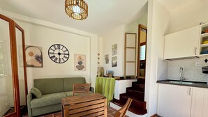 Una sala de estar con un sofá verde, una mesa de madera y una escalera que lleva a una cocina con armarios blancos.