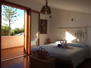 Un dormitorio con cama, una cesta de mimbre, un cuadro y vistas a árboles y al cielo.