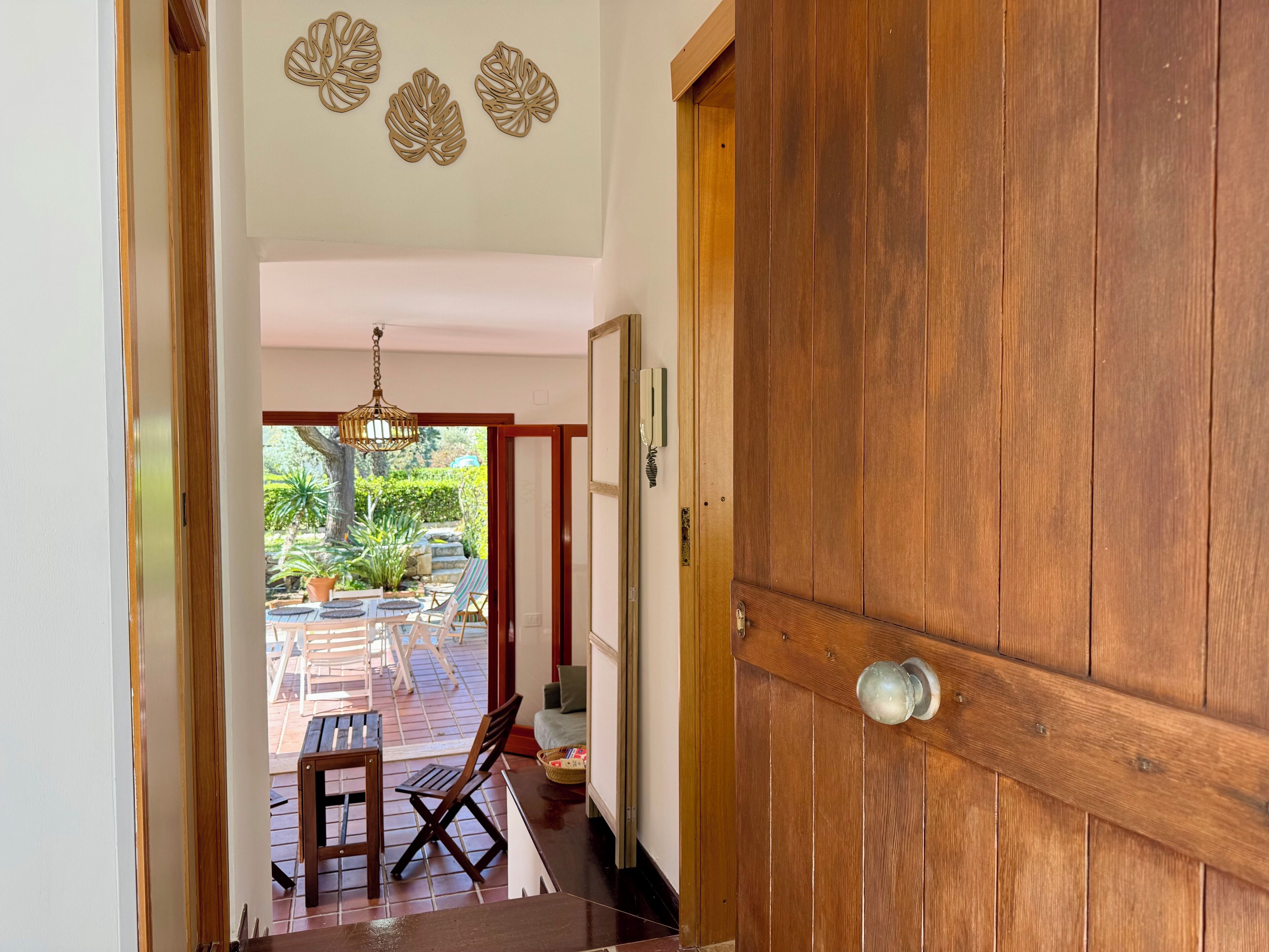 Puerta de madera que da a un patio con una mesa y sillas, una lámpara colgante y un adorno en la pared.