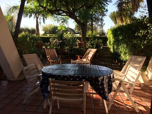 Un patio al aire libre con una mesa redonda cubierta por un mantel estampado, rodeado de sillas de madera.