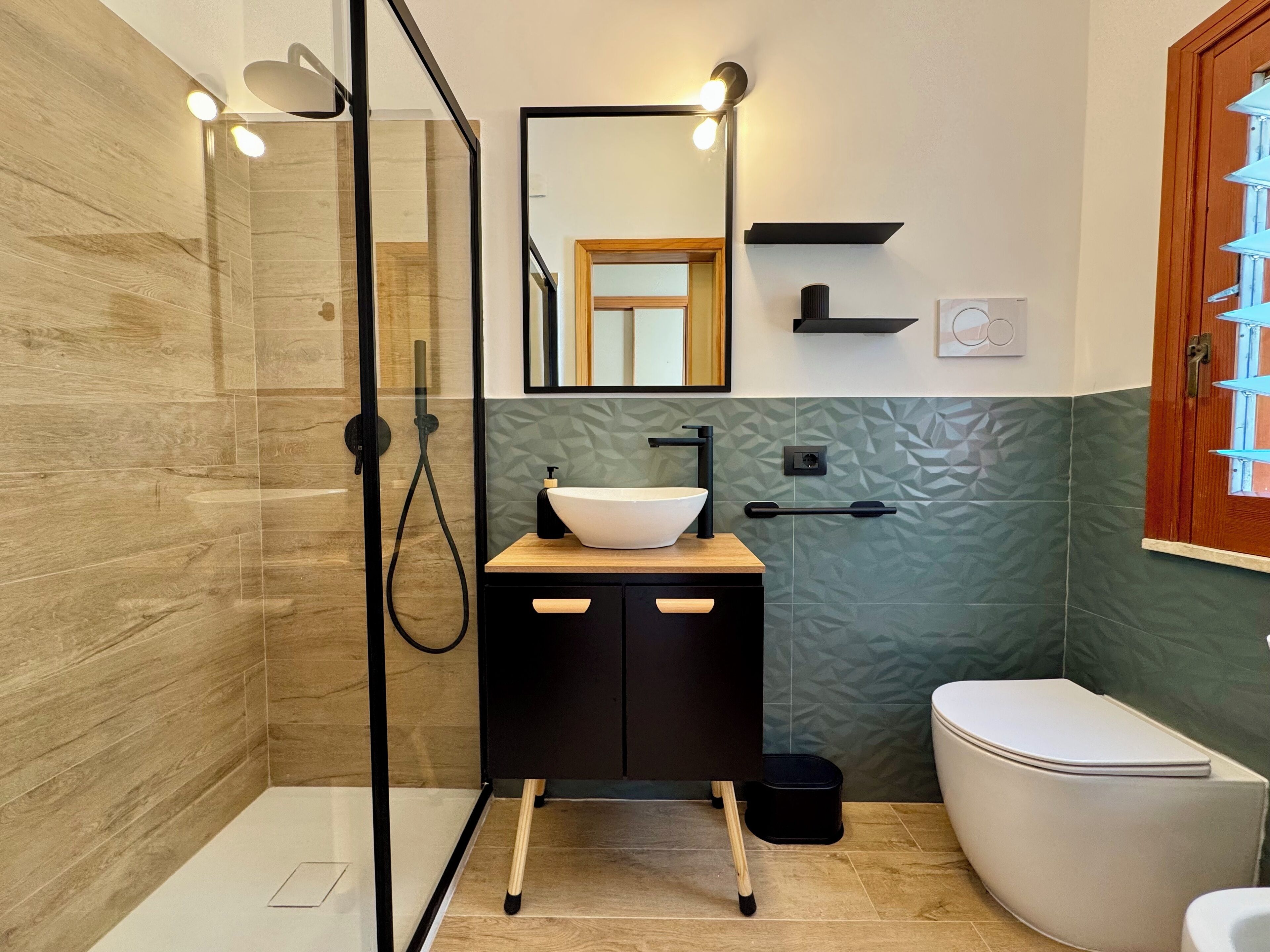 A modern bathroom with a glass shower enclosure, a wooden vanity with a white sink, and a white toilet.