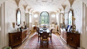 Une vaste salle à manger avec un plafond haut, des moulures décoratives et une grande fenêtre.