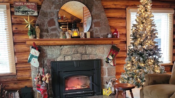 Een gezellig chaletinterieur met een stenen open haard, een kerstboom en een bord met de tekst 'HOME' aan de muur.