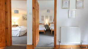 Habitación de hotel con puerta de madera, cama con ropa blanca, mesita de noche con lámpara y radiador.