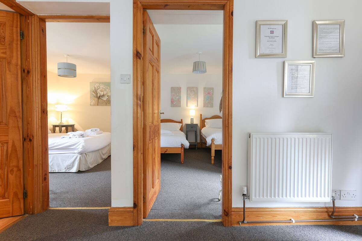 A hotel room with a wooden door, a bed with white linens, a bedside table with a lamp, and a radiator.