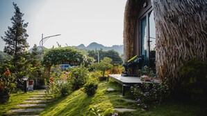 A thatched-roof structure with a wooden deck and a view of mountains in the background. - Green Homestay (Hai Phong)