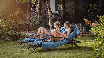 Two people relaxing on a hammock chair in a garden with a brick wall and greenery in the background.