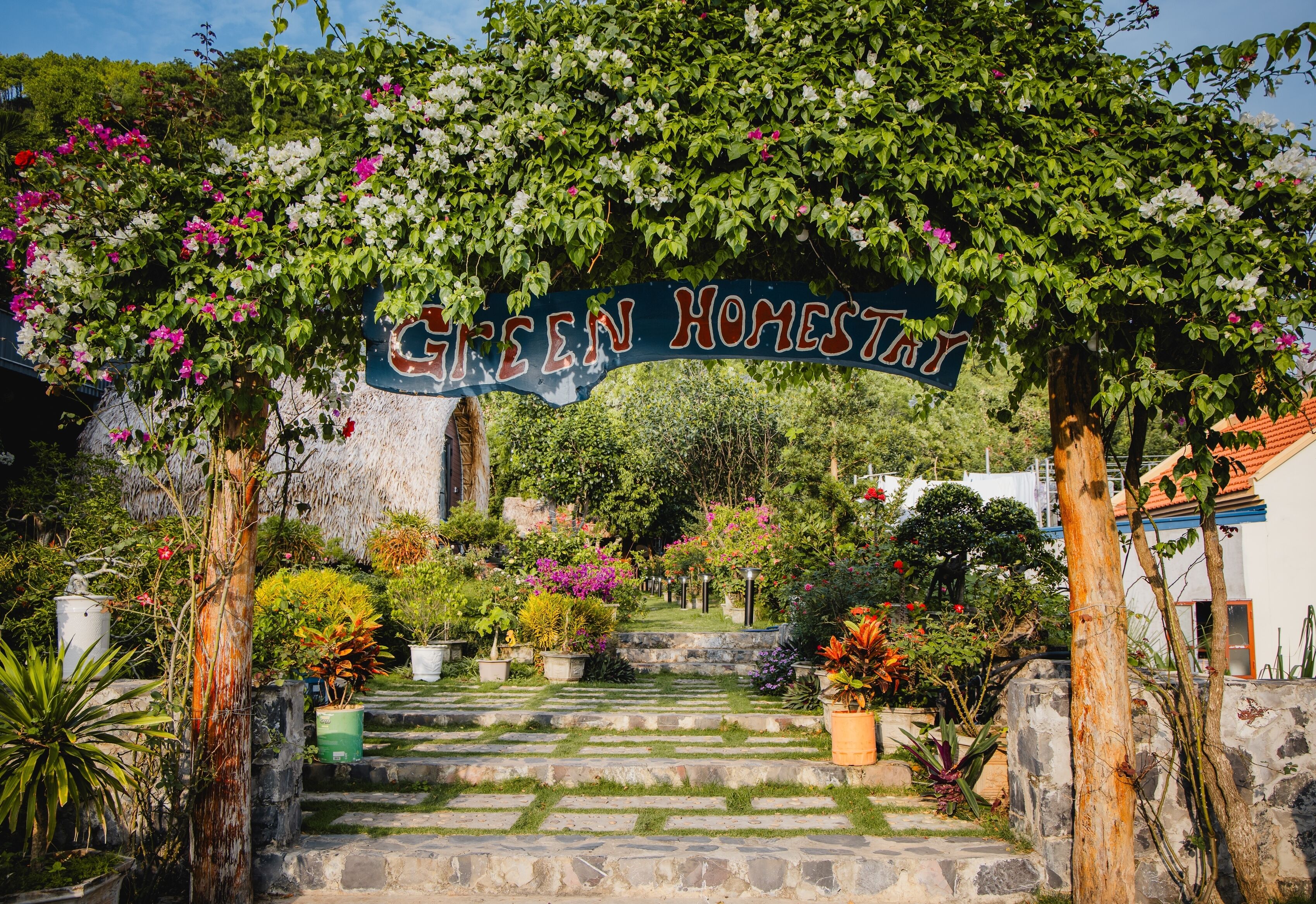 A garden entrance with a sign reading "Green Homestay" and stone steps leading up to it.