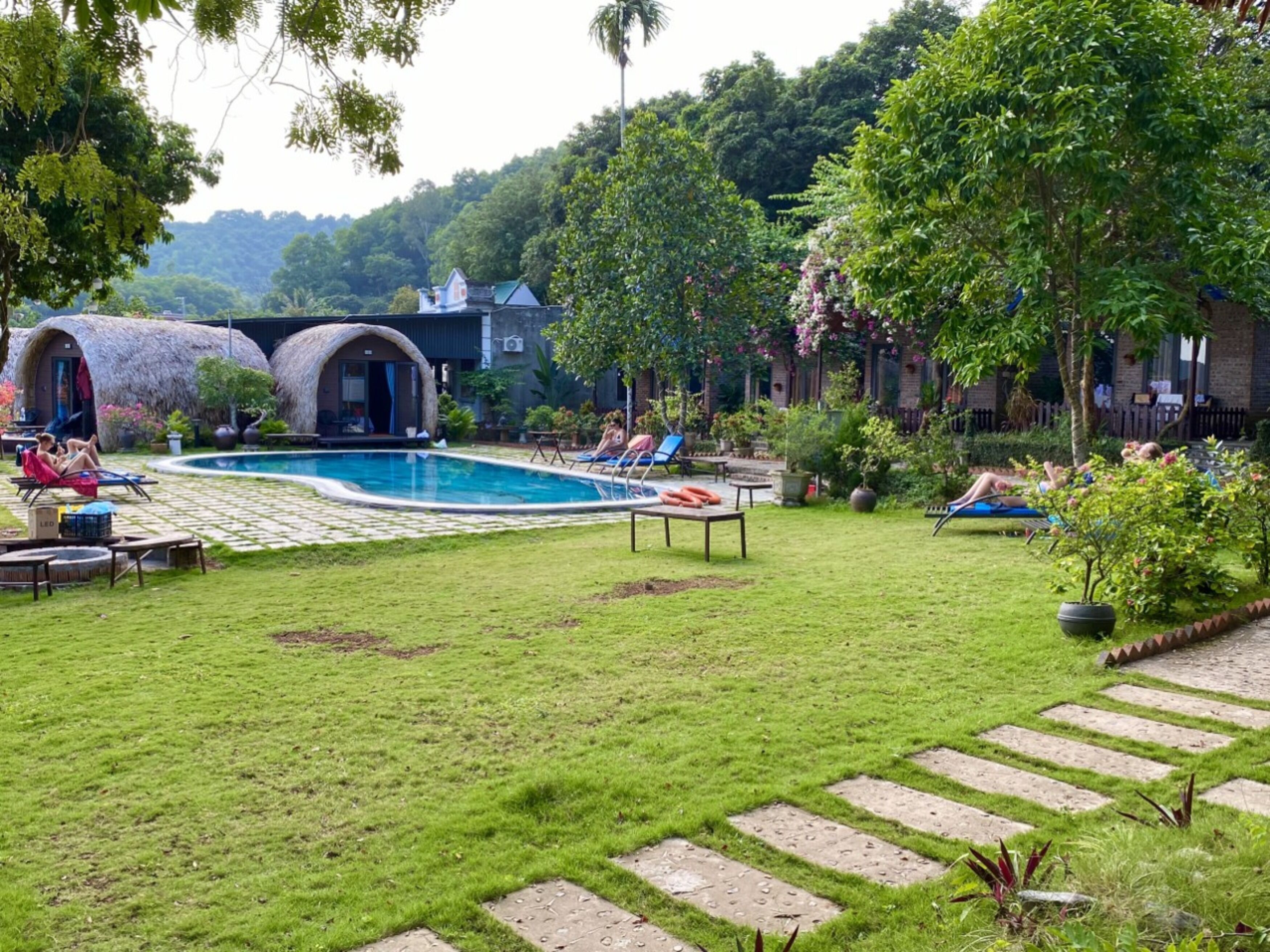 A pool area with lounge chairs, a thatched-roof structure, and a well-maintained lawn.