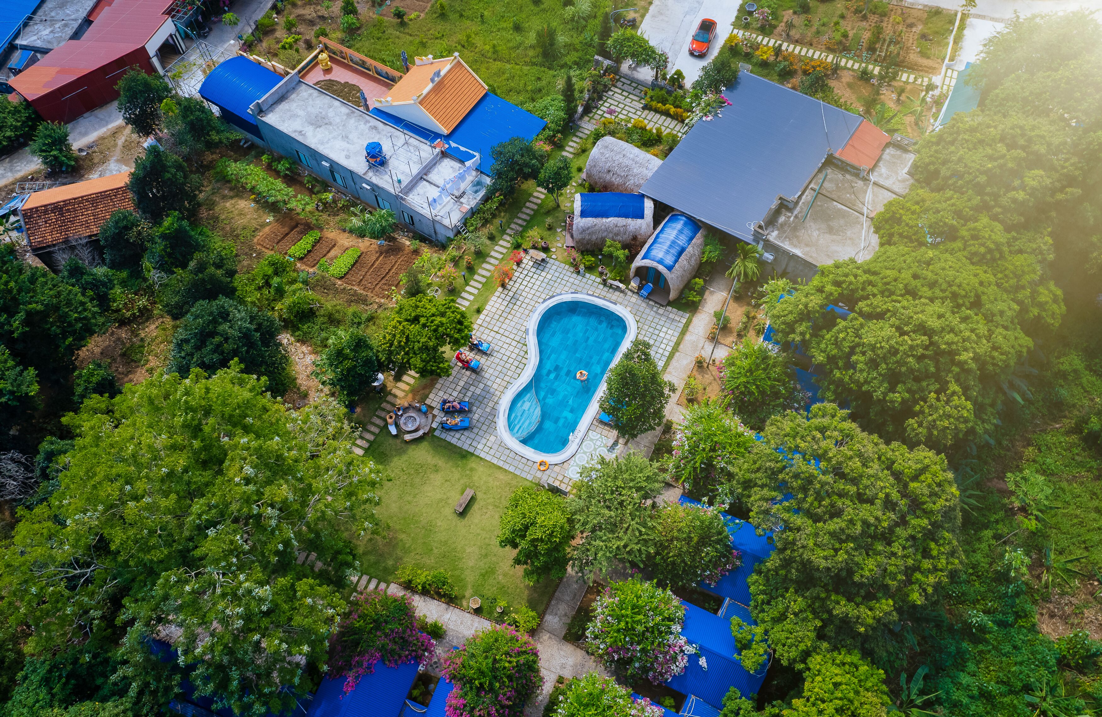 An aerial view of a residential area with a swimming pool surrounded by lush greenery and various buildings.