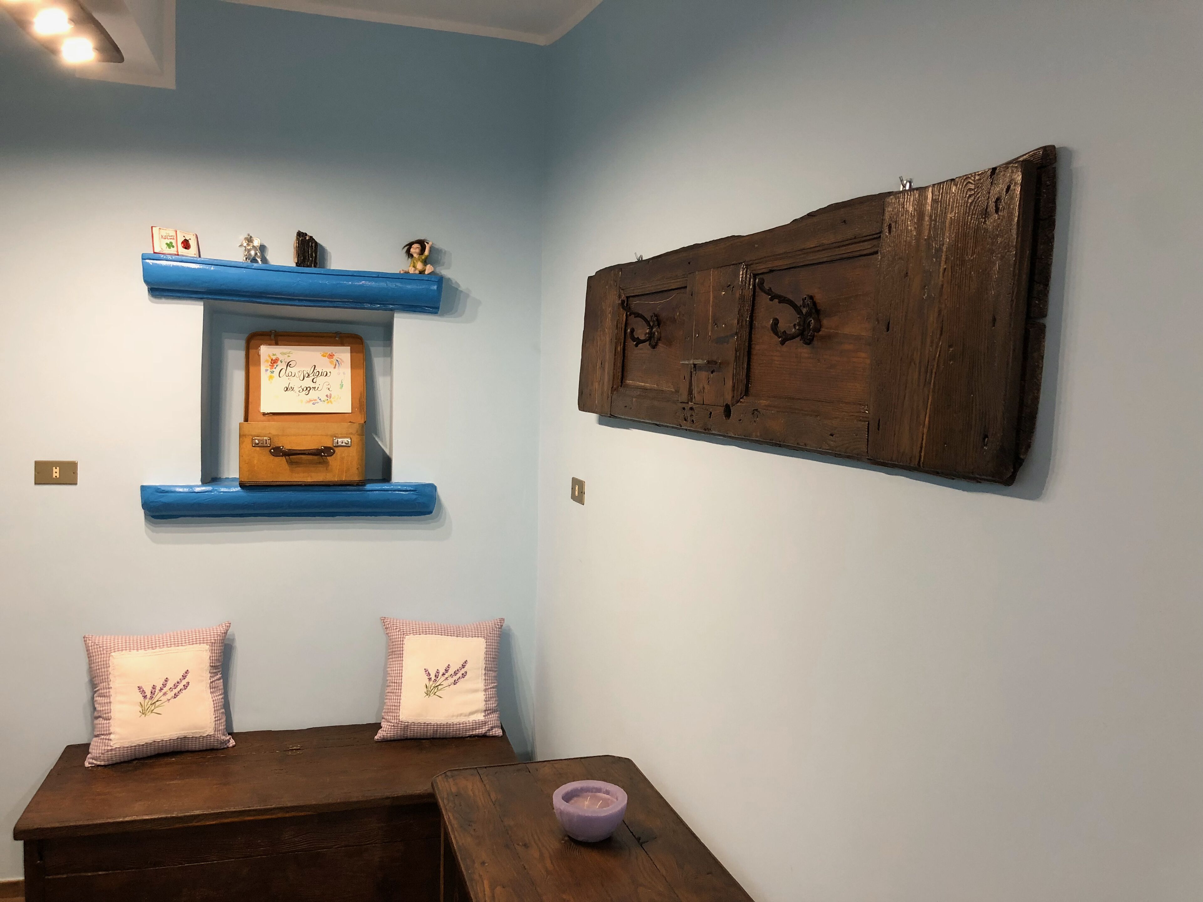 A room with a blue wall, a wooden chest of drawers, a wooden cabinet, and two decorative pillows.