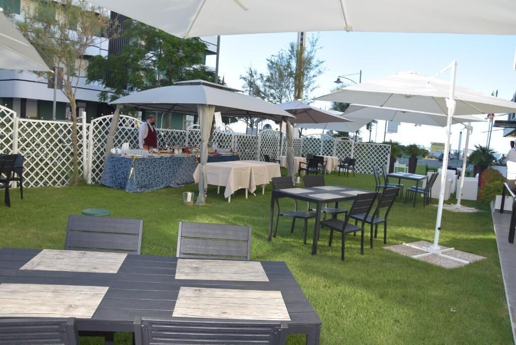 Un patio al aire libre con mesas y sillas bajo sombrillas blancas, rodeado por una cerca de celosía blanca.