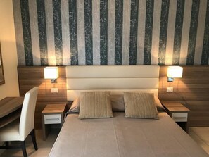 Een moderne hotelkamer met een groot bed, twee nachtkastjes, een bureau en een stoel.