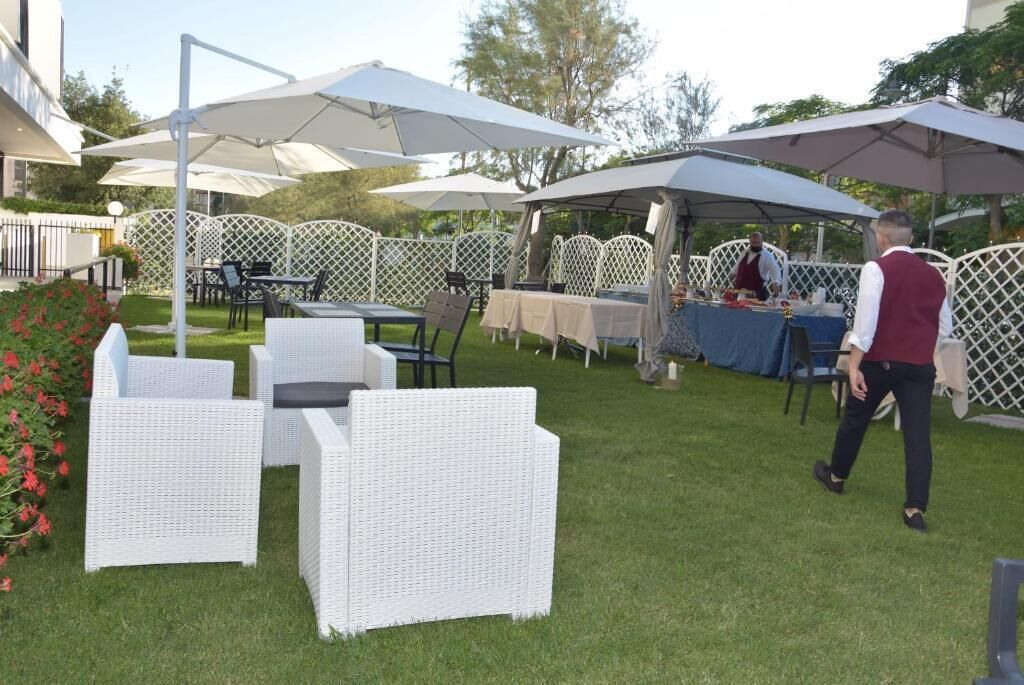 An outdoor patio area with white wicker furniture, umbrellas, and a table set up for dining.