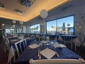 Un restaurante con mesas preparadas para comer, ventanas amplias y vista al exterior.