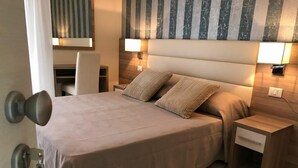 Un lit bien fait, avec une tête de lit, deux tables de chevet avec des lampes et une porte dotée d’une poignée.