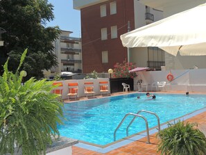 Una piscina con plataforma de baldosas, rodeada de sillas de descanso y sombrillas.