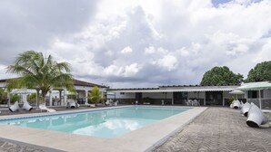 A swimming pool with lounge chairs and umbrellas, surrounded by a covered patio area with tables and chairs. - Hotel Turistico de Alagoinhas (Alagoinhas)