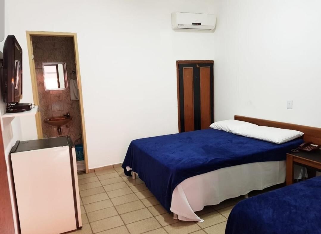 Quarto pequeno e limpo com duas camas, televisão, frigorífico e casa de banho.