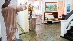 A statue of a person in a room with a tiled floor, a bench, a table with a vase, and a painting on the wall. - Hotel Turistico de Alagoinhas (Alagoinhas)
