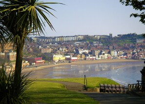 A coastal town with a beach, buildings, and a hill in the background.