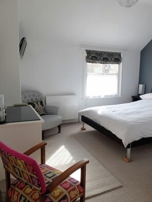 A bedroom with a bed, a desk, a chair, a radiator, and a window.