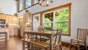 A rustic kitchen with wooden cabinets, a large dining table, and a view of greenery through large windows. - A Mornings Mist - Morganton, GA (Morganton)