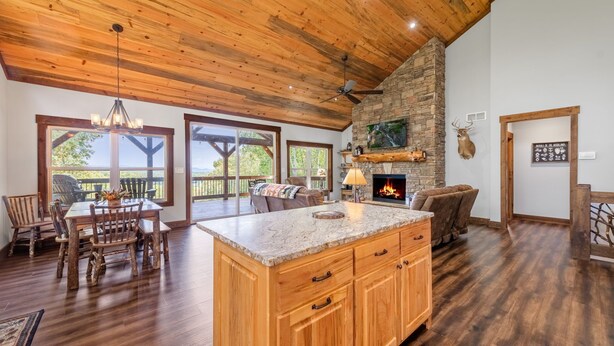 A spacious kitchen with a large island, wooden ceiling, stone fireplace, and a view through large windows. - A Mornings Mist - Morganton, GA (Morganton)