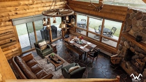 Un intérieur spacieux de chalet en bois, comprenant un coin repas, des sièges et de grandes fenêtres donnant sur une rivière.
