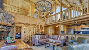 L’intérieur de cette vaste cabane en rondins est agrémenté d’une cheminée en pierre, d’un coin repas en bois, d’un canapé en cuir et d’une cuisine dotée de meubles en bois.
