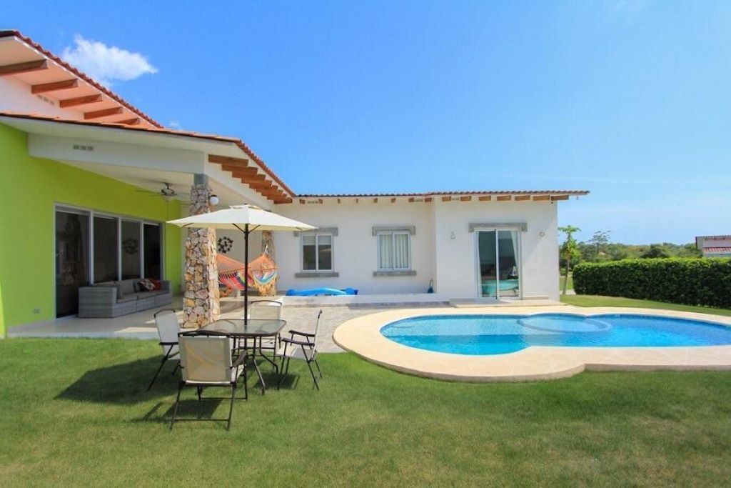A house with a swimming pool, a patio with chairs and a table, and a covered outdoor area.