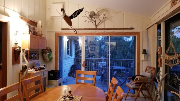 Een eetruimte met een houten tafel en stoelen, een kroonluchter en uitzicht door een schuifdeur op een terras.