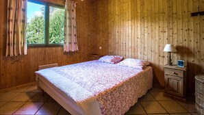 A wooden cabin bedroom with a bed, curtains, a nightstand, and a lamp.