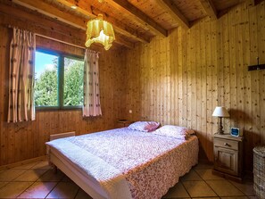 A wooden cabin bedroom with a bed, curtains, a nightstand, and a lamp.