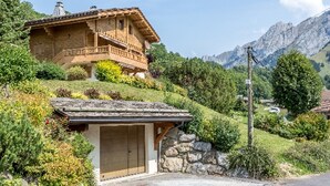 A wooden chalet with a balcony, a garage, and a stone wall.