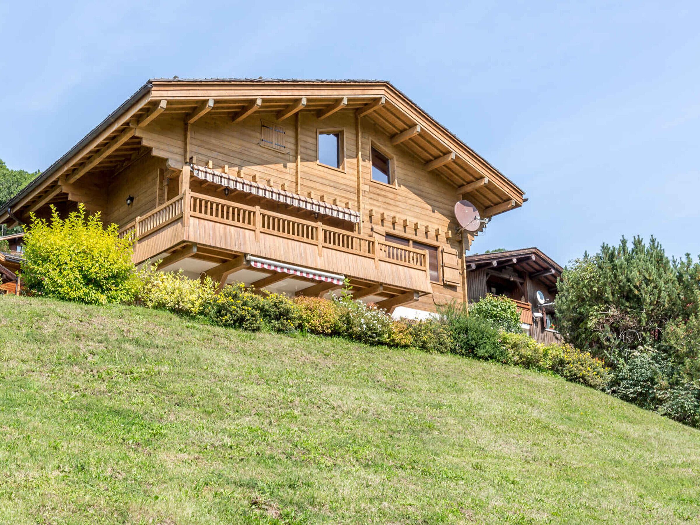 A wooden chalet with a balcony, situated on a grassy hillside.