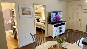 A living room with a television, a dining table with chairs, a kitchen area, and a bathroom visible through an open door. - Unique space on WTAMU campus. Walk to anything and everything! (Canyon)