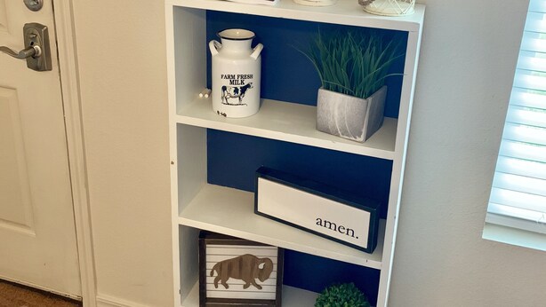 A white shelf with a 'Welcome Guests' sign, a book titled 'Fresh Rock', a white mug labeled 'Farm Fresh Milk', a framed picture of a bull, and a small plant. - Unique space on WTAMU campus. Walk to anything and everything! (Canyon)