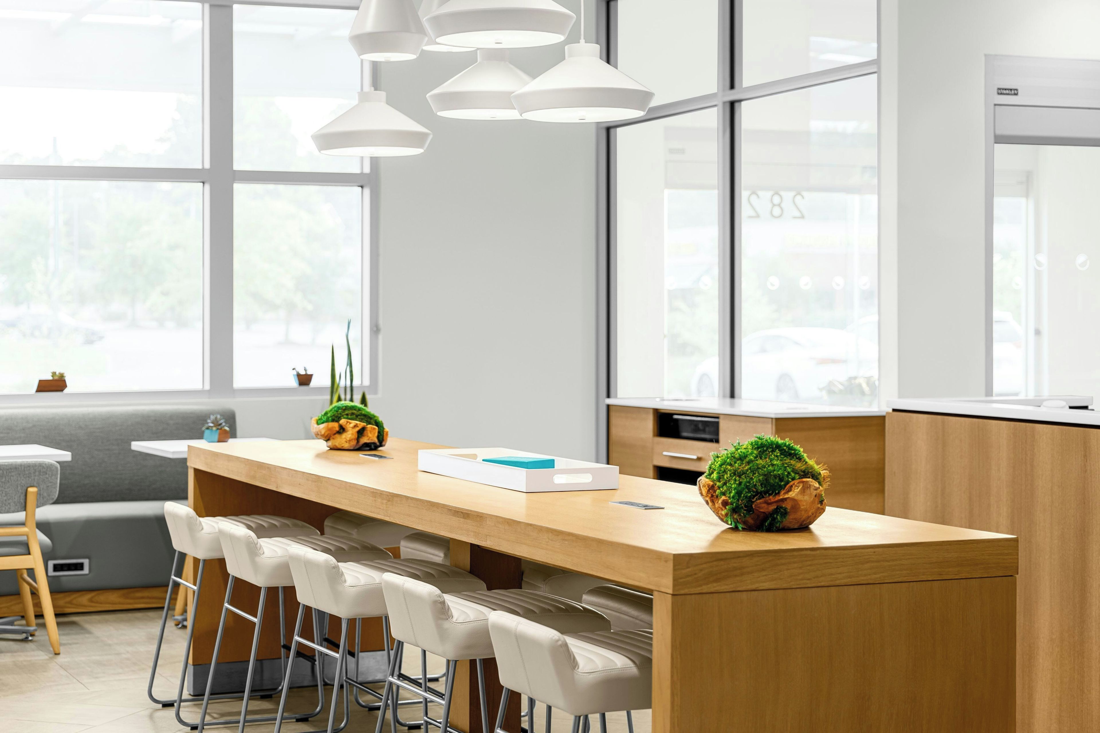 A modern kitchen with a wooden island, bar stools, pendant lights, and large windows.