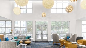 Eine geräumige Lobby mit einer großen Eckcouch, mehreren Sesseln und einem Couchtisch. Große Fenster sorgen für natürliches Licht und einen Blick ins Freie.