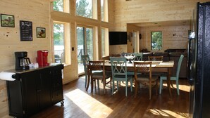 A wooden cabin interior with a dining area, kitchen, and large windows. - Paradise Shores & Fish Galore ~your own private beach & dock! (Cable)