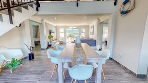 A spacious dining area with a long wooden table and modern chairs, leading to a kitchen and a living area with a staircase. - Caribbean Estate Deluxe (Port Edward)